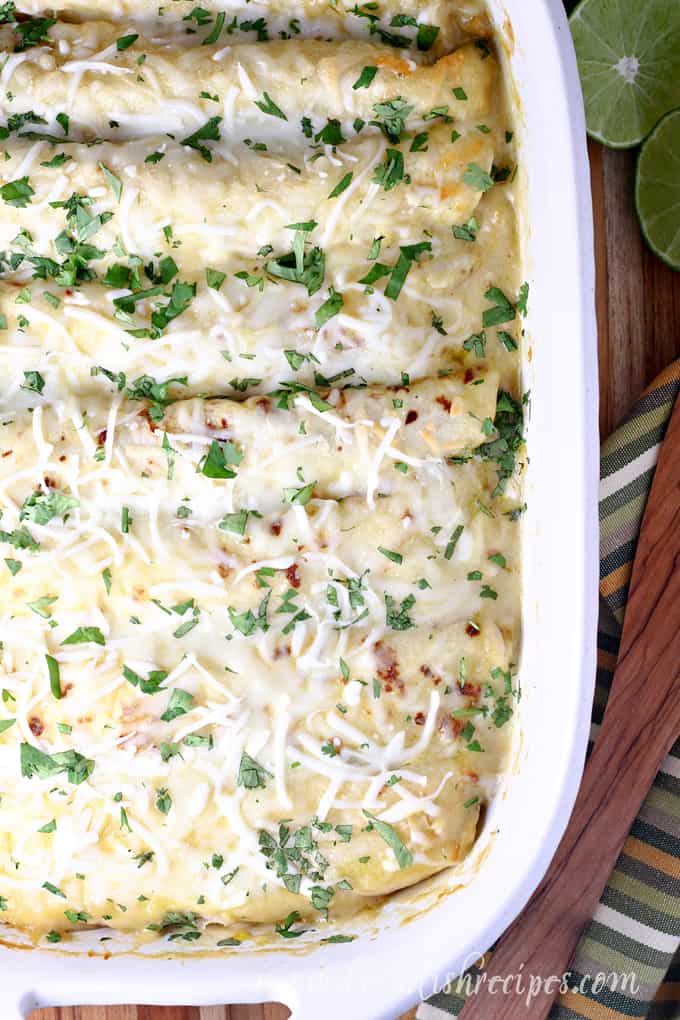 Pan of pulled pork enchiladas topped with green chili sauce and cheese.