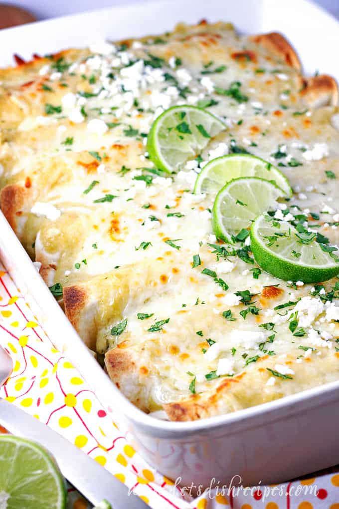 Pan of enchiladas filled with street corn and cheese, topped with lime wedges.